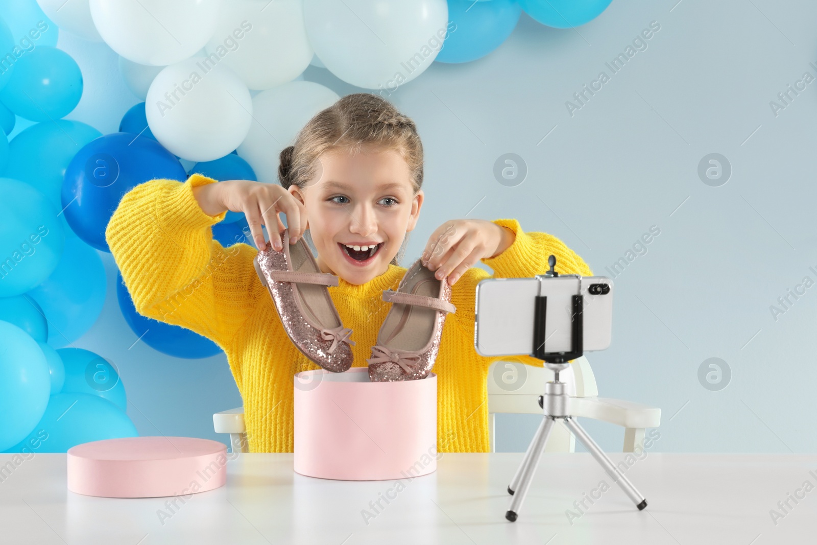 Photo of Excited little blogger with shoes recording video at table