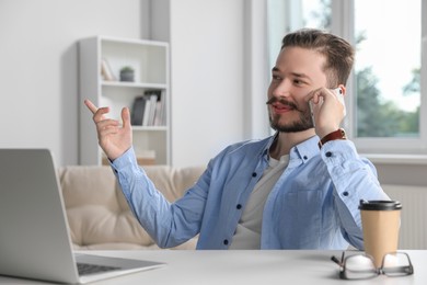 Photo of Happy man talking on smartphone while working in office
