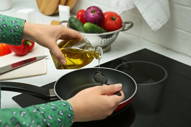 Photo of Woman pouring oil from jug into pan in kitchen, closeup