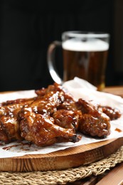 Photo of Tasty chicken wings and mug of beer on wooden table, closeup. Delicious snack