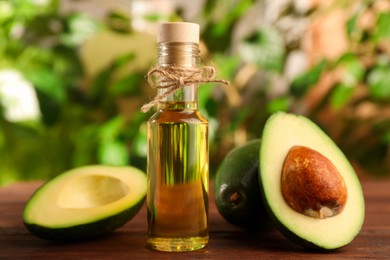 Photo of Glass bottlecooking oil and fresh avocados on wooden table against blurred green background