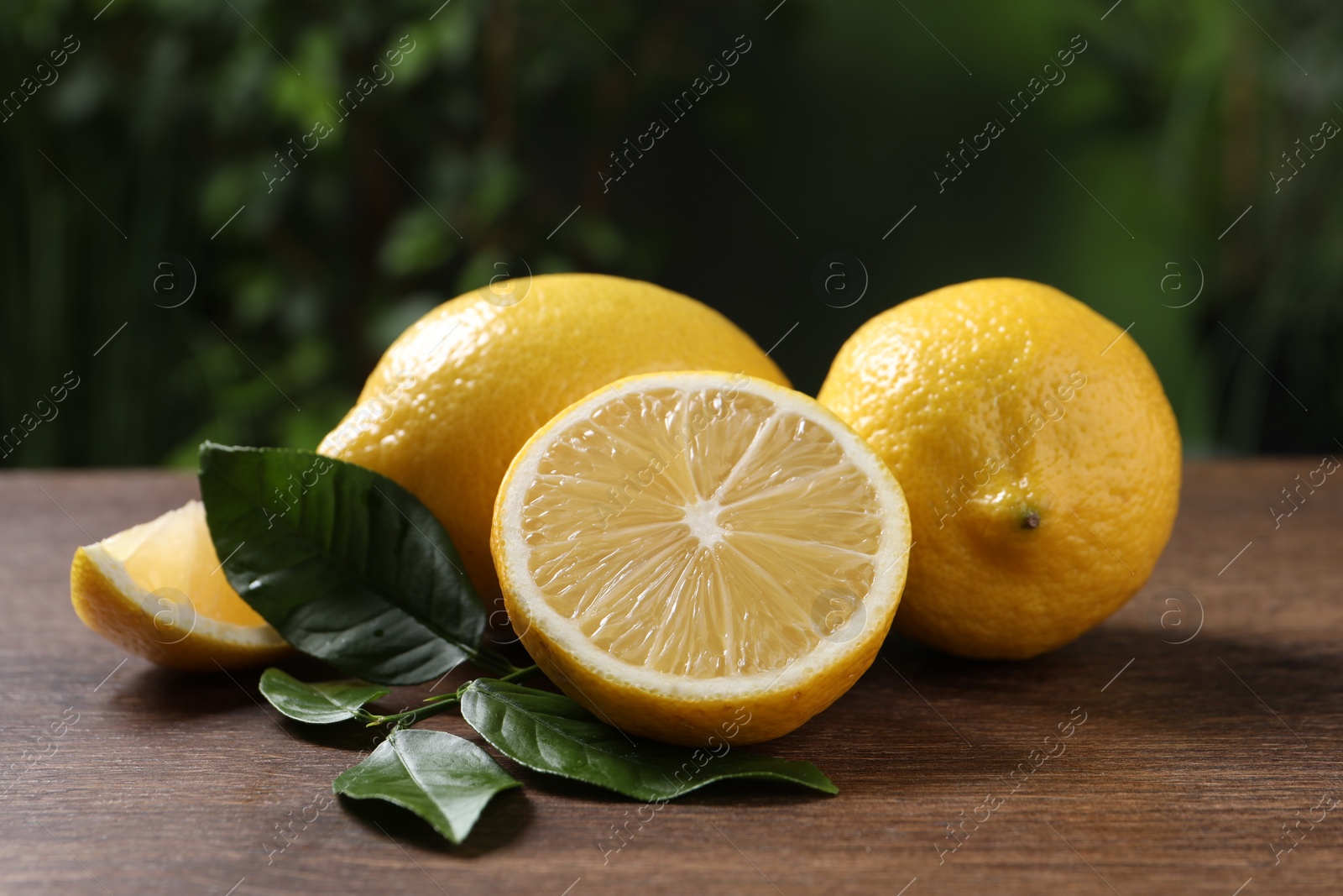 Photo of Fresh lemons and green leaves on wooden table outdoors, closeup