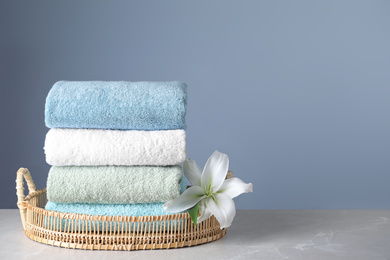 Photo of Wicker tray with folded bath towels and beautiful flower on grey table. Space for text