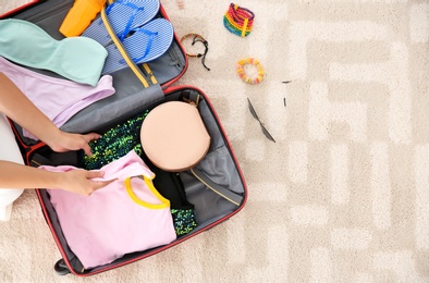 Photo of Young woman packing suitcase for summer journey at home, top view