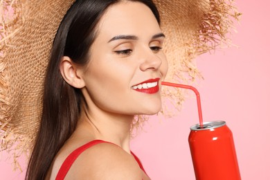 Photo of Beautiful young woman with straw hat drinking from tin can on pink background, closeup