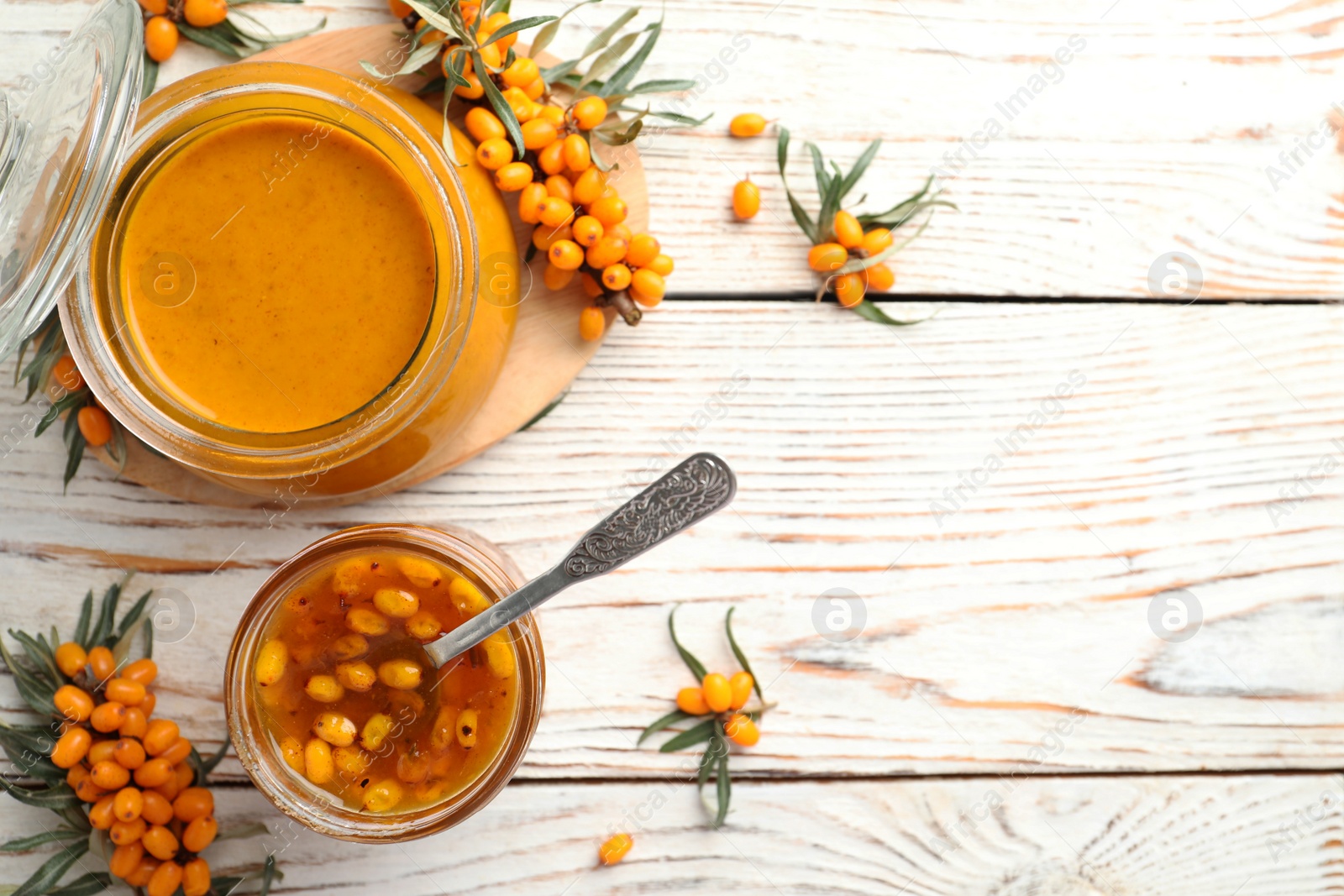 Photo of Delicious sea buckthorn jam and fresh berries on white wooden table, flat lay. Space for text