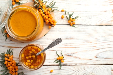 Delicious sea buckthorn jam and fresh berries on white wooden table, flat lay. Space for text