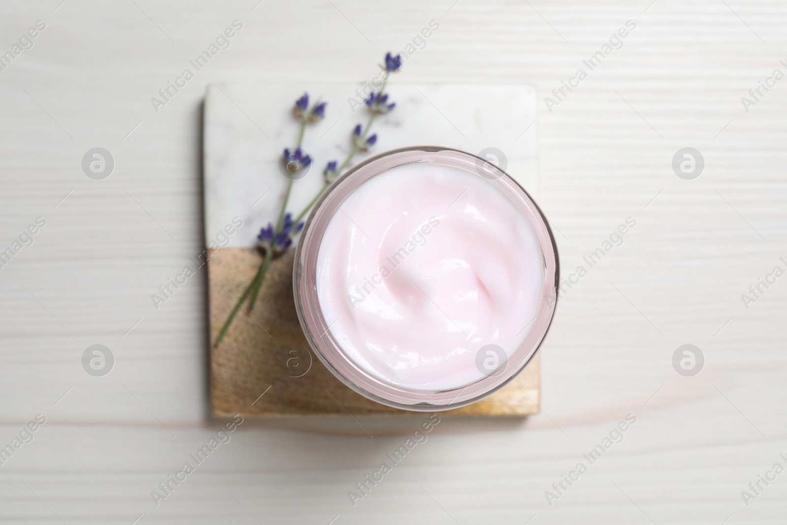 Photo of Jar of hand cream and lavender flowers on white wooden table, top view