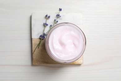 Photo of Jar of hand cream and lavender flowers on white wooden table, top view