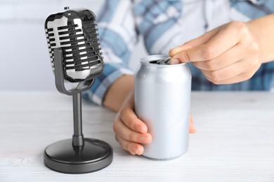 Photo of Woman making ASMR sounds with microphone and can at white table, closeup