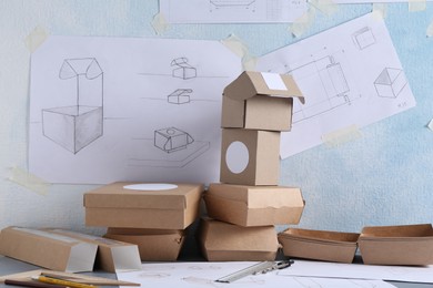 Photo of Creating packaging design. Drawings, boxes and stationery on table, closeup