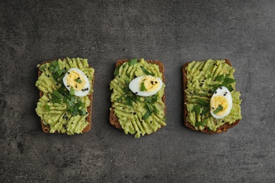Photo of Tasty crisp rye toasts with avocado and quail egg on table, flat lay
