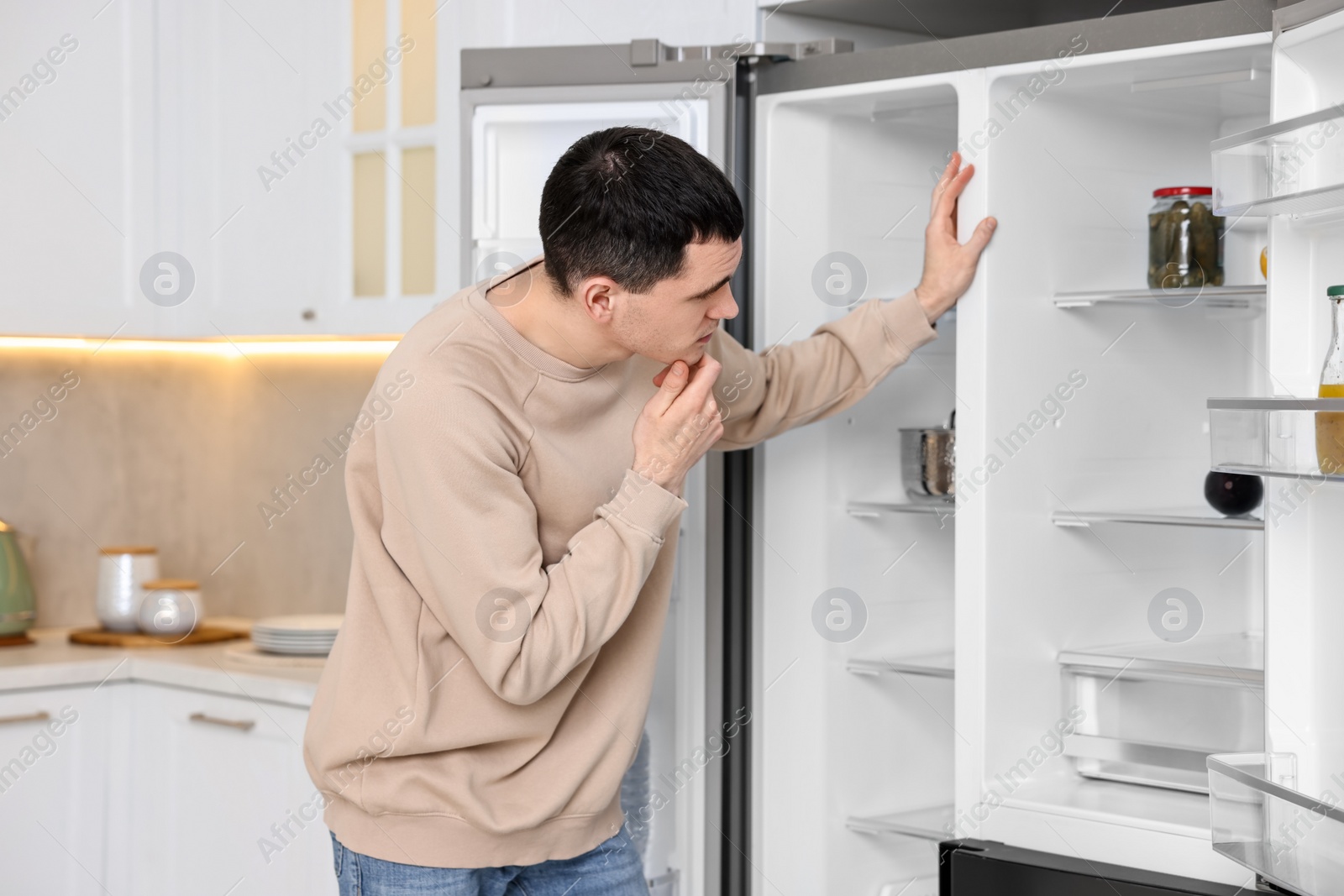 Photo of Thoughtful man near empty refrigerator in kitchen at home