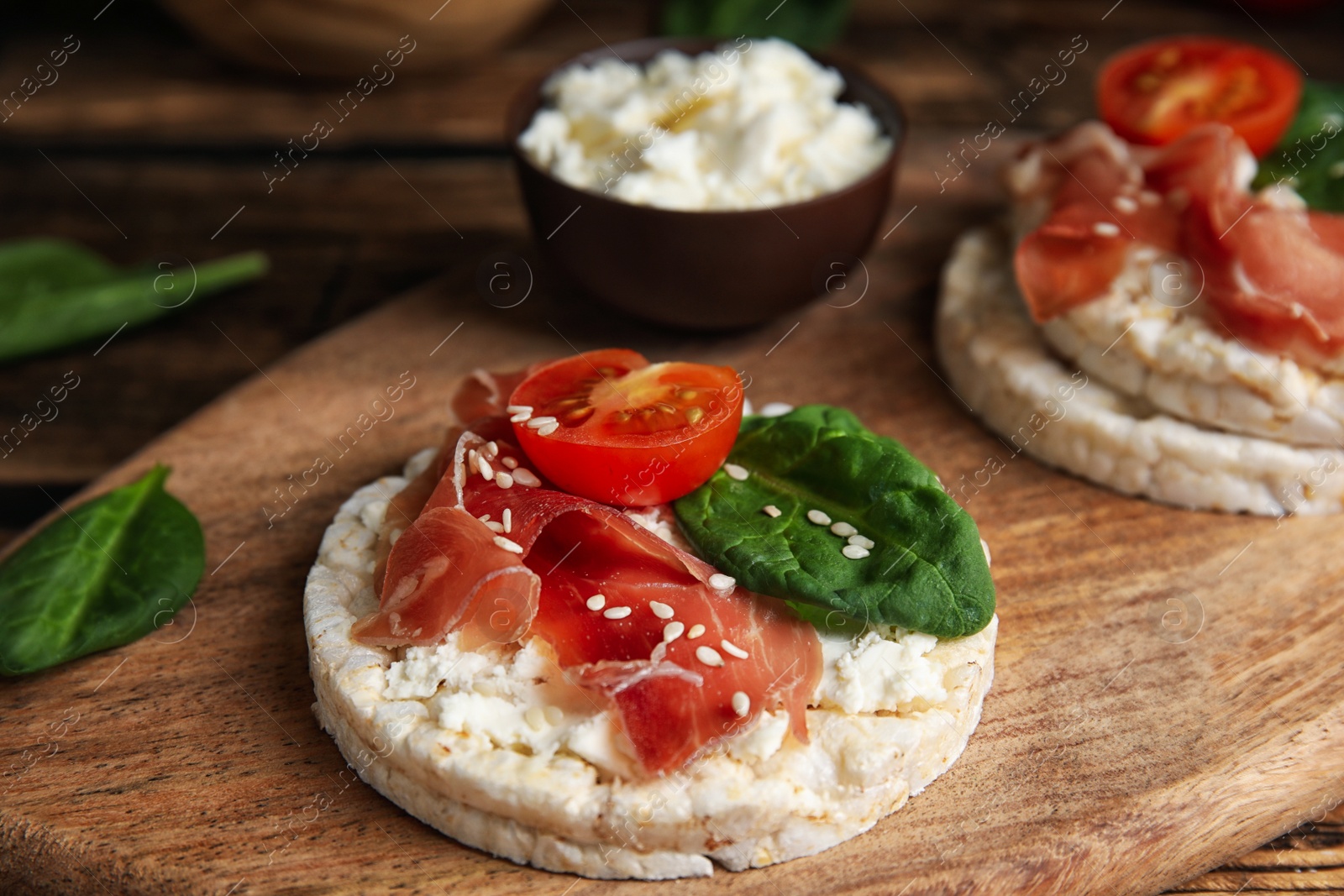 Photo of Puffed rice cake with prosciutto, tomato and basil on wooden board, closeup