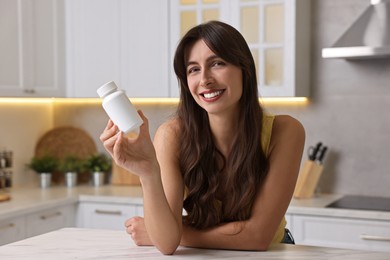 Photo of Beautiful woman with bottle of vitamin pills at white marble table in kitchen