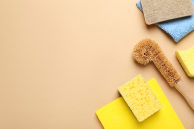 New sponges, rags and brush on beige background, flat lay. Space for text