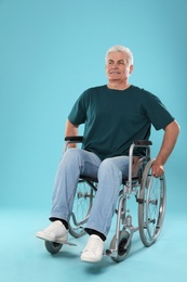 Senior man in wheelchair on color background