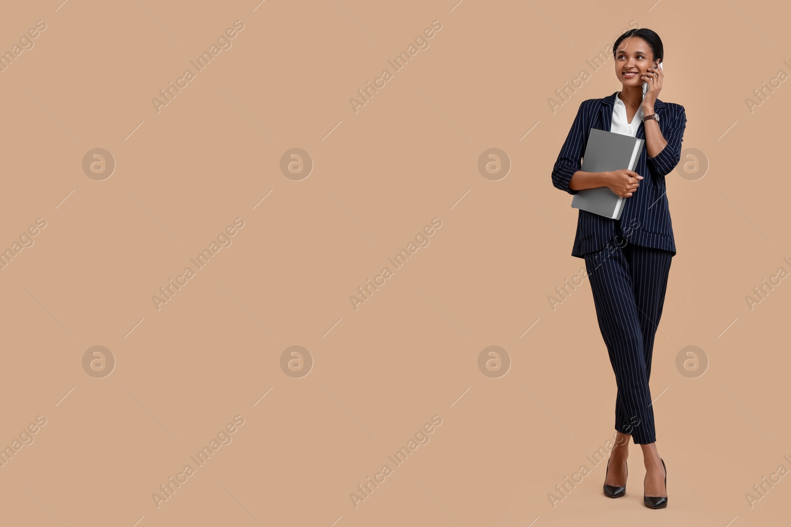 Photo of Beautiful secretary with folder talking on phone against beige background, space for text