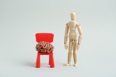 Photo of Mini chair with brain made of plasticine and wooden human model on white background