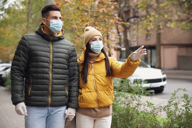 Photo of Couple in medical face masks and gloves walking outdoors. Personal protection during COVID-19 pandemic