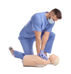 Photo of Doctor in uniform and protective mask practicing first aid on mannequin against white background