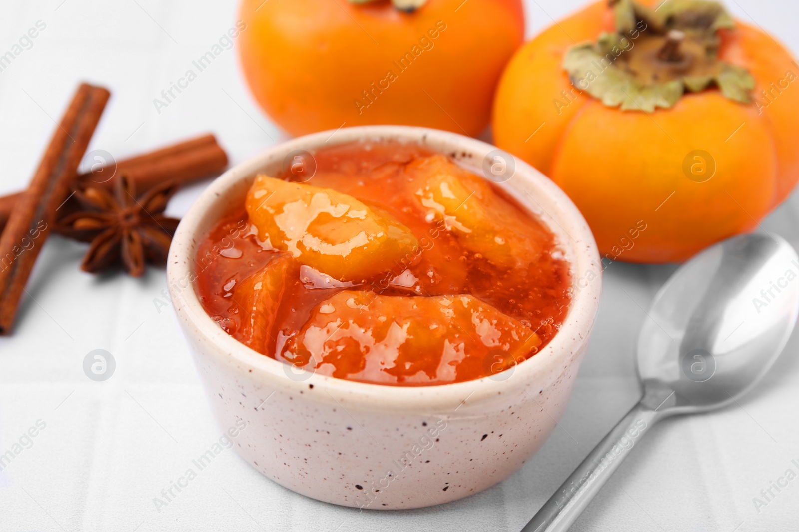 Photo of Bowl of tasty persimmon jam and ingredients on white tiled table