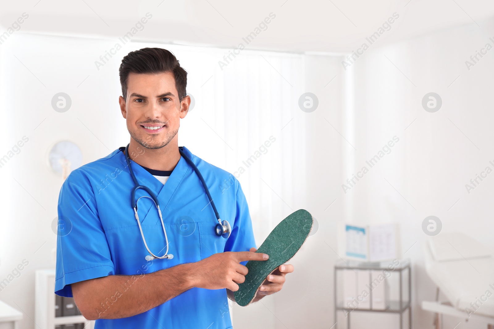 Photo of Handsome male orthopedist showing insole in clinic