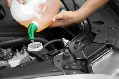 Man pouring liquid from plastic canister into car washer fluid reservoir, closeup