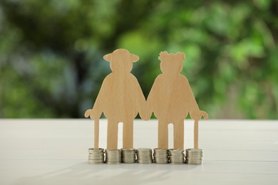 Pension savings. Figure of senior couple and coins on white table against blurred green background