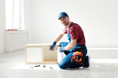 Photo of Handyman in uniform assembling furniture indoors. Professional construction tools