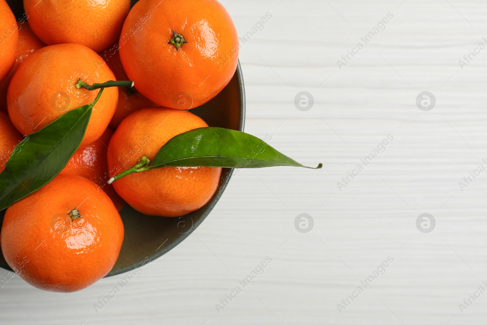 Photo of Delicious tangerines with green leaves in bowl on white wooden table, top view. Space for text