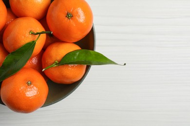 Delicious tangerines with green leaves in bowl on white wooden table, top view. Space for text