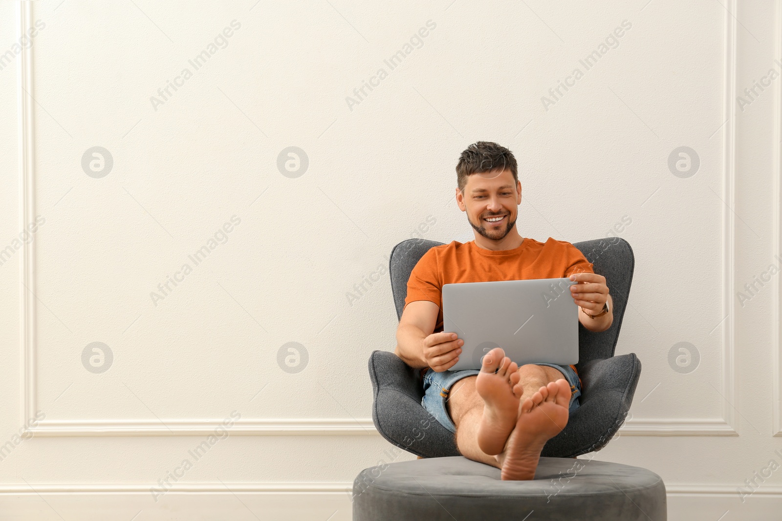 Photo of Happy man using laptop in armchair indoors, space for text. Internet shopping