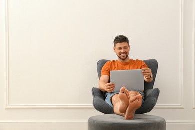 Photo of Happy man using laptop in armchair indoors, space for text. Internet shopping