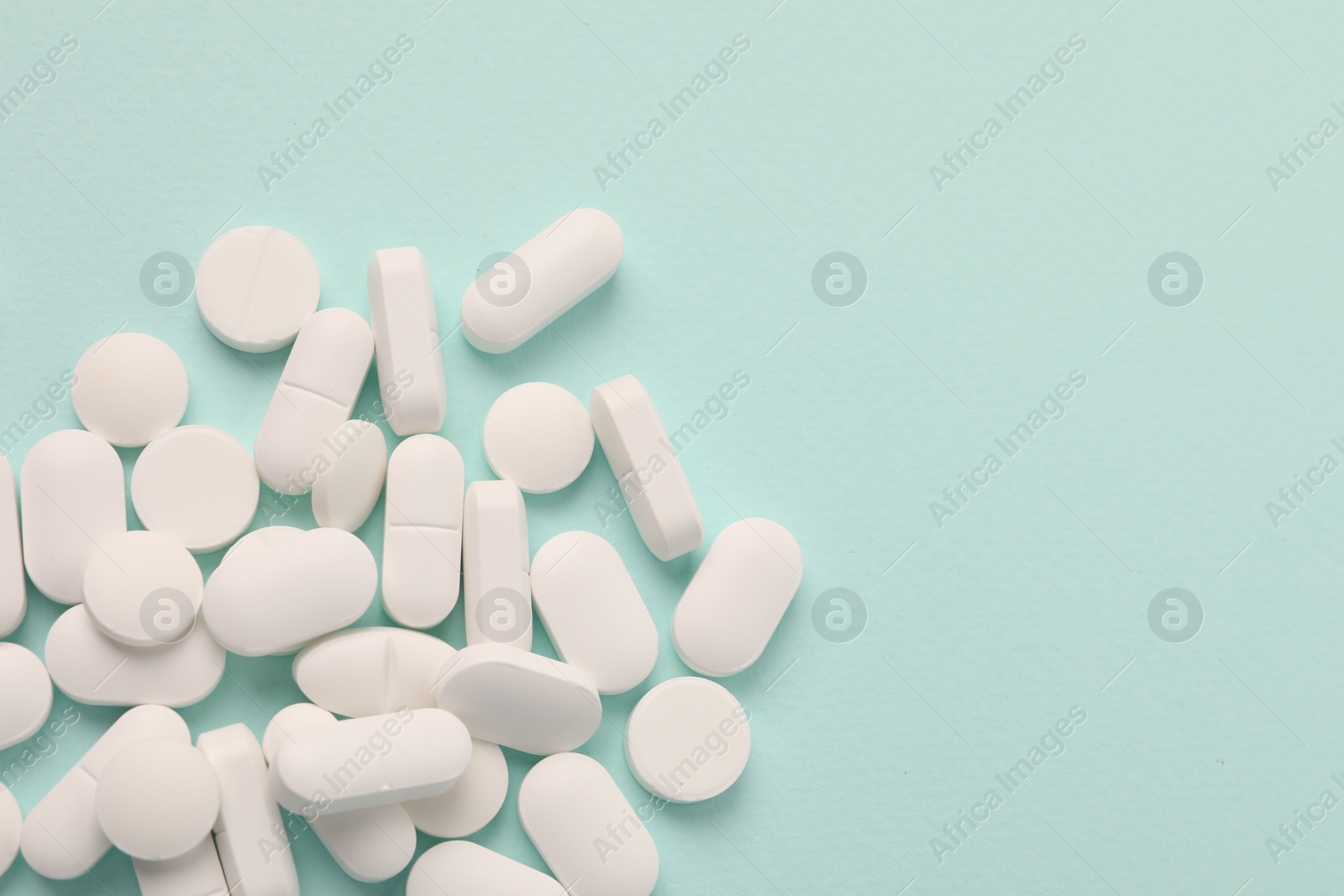 Photo of Pile of white pills on mint background, flat lay. Space for text