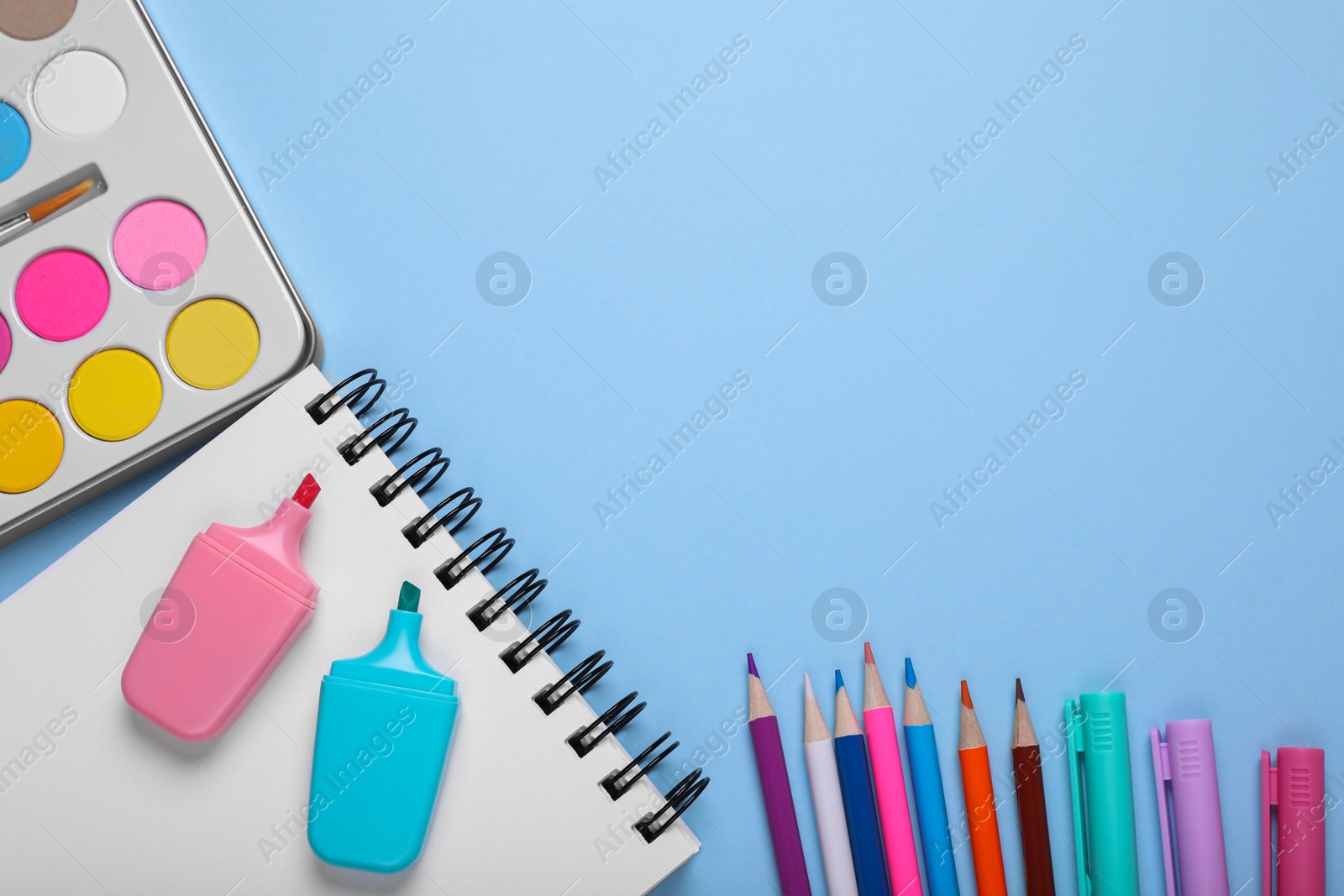 Photo of Watercolor palette, colorful pencils and markers on light blue background, flat lay. Space for text