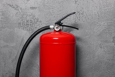 Red fire extinguisher near grey wall, closeup
