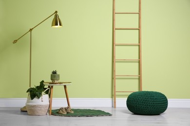 Photo of Stylish room interior with comfortable knitted pouf and plants near light green wall