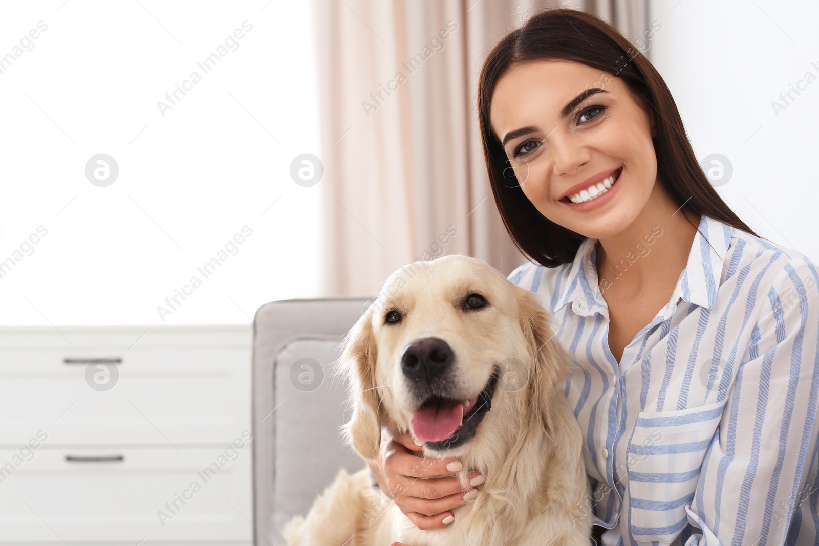 Photo of Young woman and her Golden Retriever dog in living room. Space for text