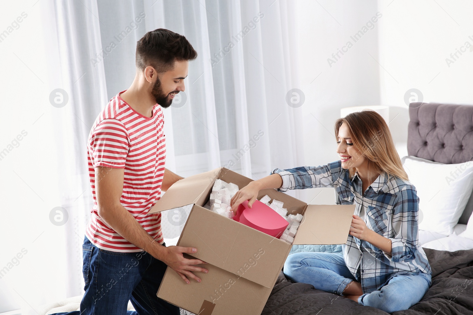 Photo of Young couple opening parcel in bedroom at home