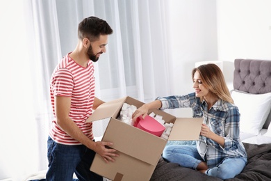 Young couple opening parcel in bedroom at home