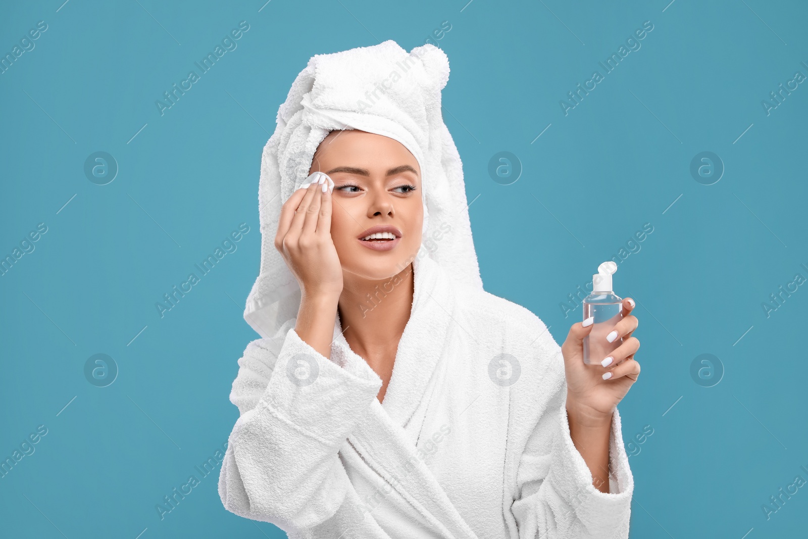 Photo of Beautiful woman removing makeup with cotton pad on light blue background