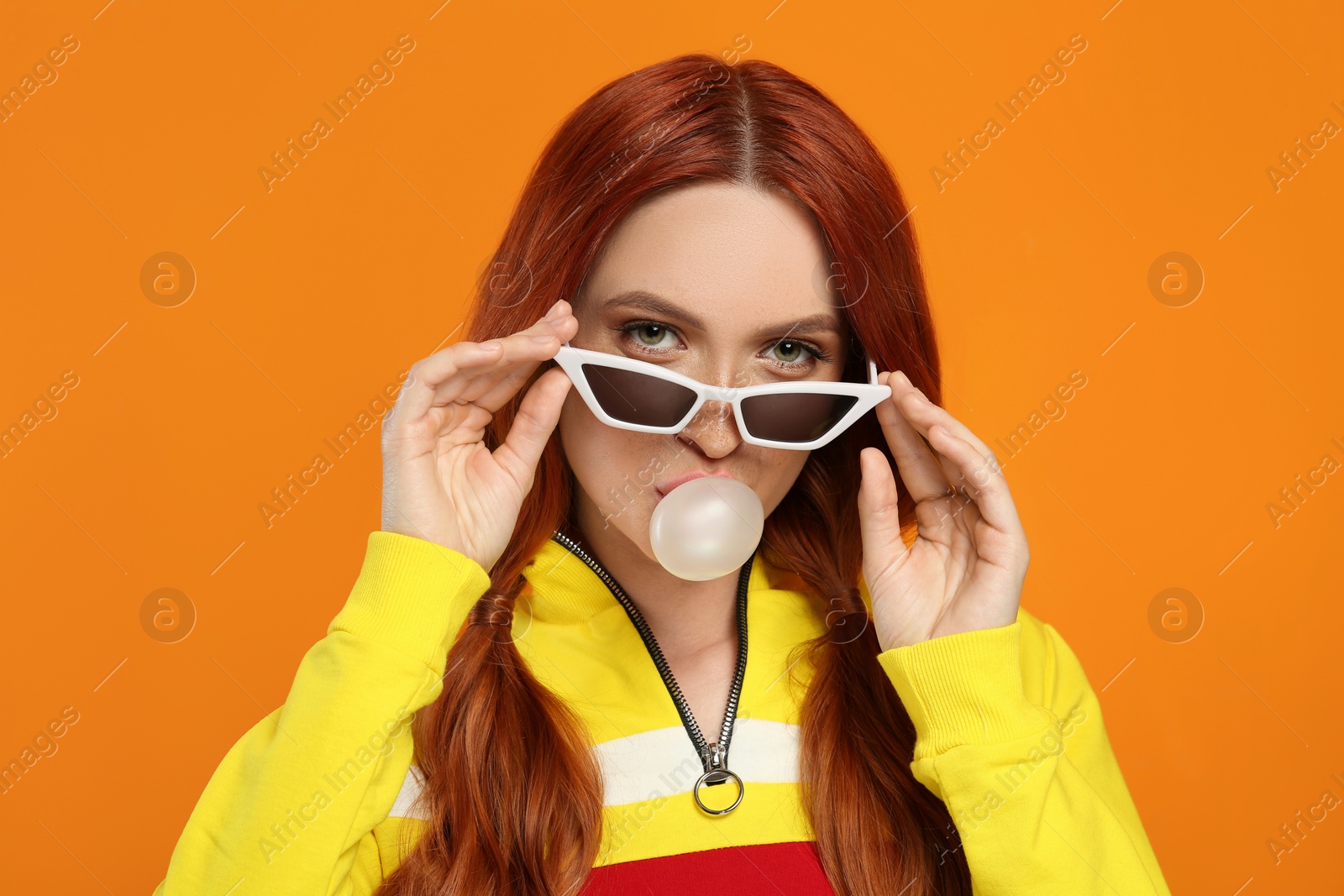 Photo of Portrait of beautiful woman in sunglasses blowing bubble gum on orange background