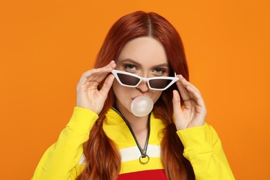 Photo of Portraitbeautiful woman in sunglasses blowing bubble gum on orange background