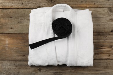 Photo of Black karate belt and white kimono on wooden background, top view