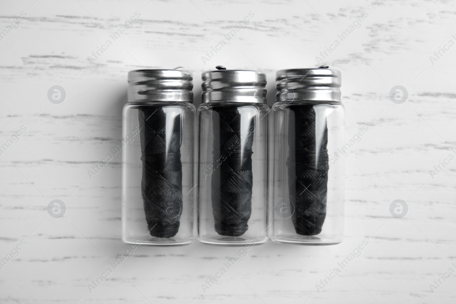 Photo of Biodegradable dental flosses in glass jars on white wooden background, flat lay