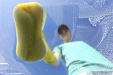 Photo of Woman cleaning glass with sponge on sunny day