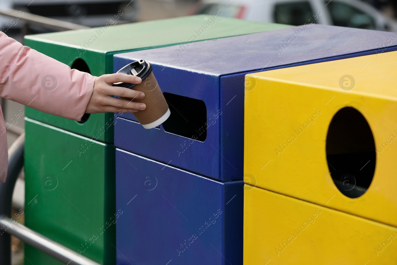 Photo of Woman throwing paper coffee cup into garbage bin outdoors, closeup. Waste sorting