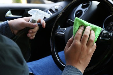 Photo of Man cleaning steering wheel with rag and spray bottle in car, closeup