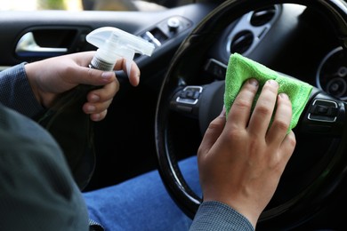 Man cleaning steering wheel with rag and spray bottle in car, closeup